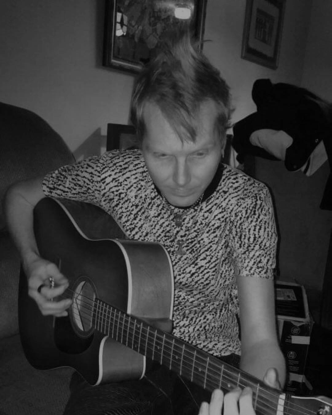 Ian Payson playing an acoustic guitar, photographed in black and white