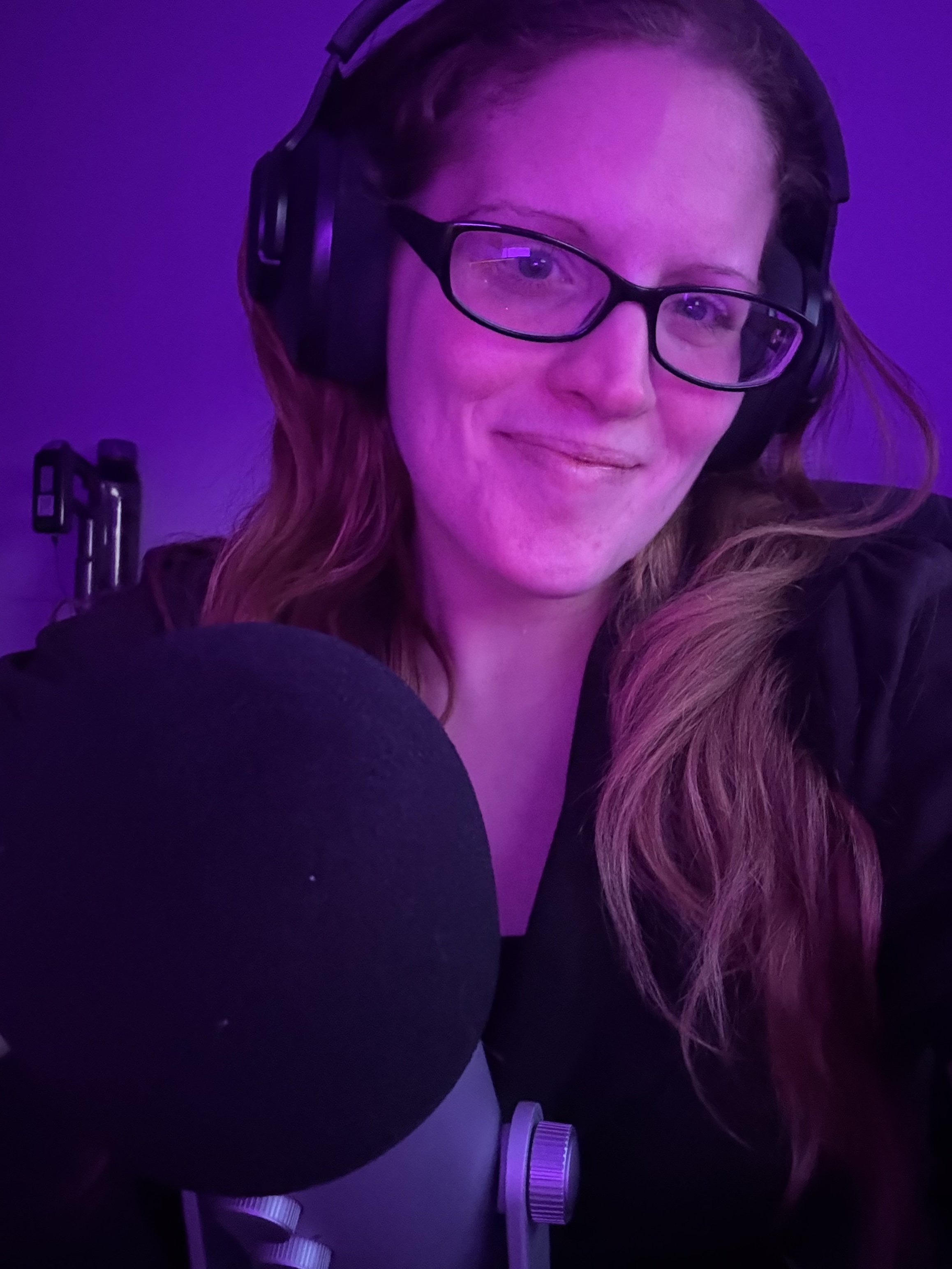 Authentic portrait of Miki Byrne wearing glasses and headphones beside a recording microphone